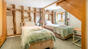 A bedroom with two beds, wooden beams on the walls, a small table, and a window with curtains. - 3 Bed in Chediston (oc-b43313) (Chediston)
