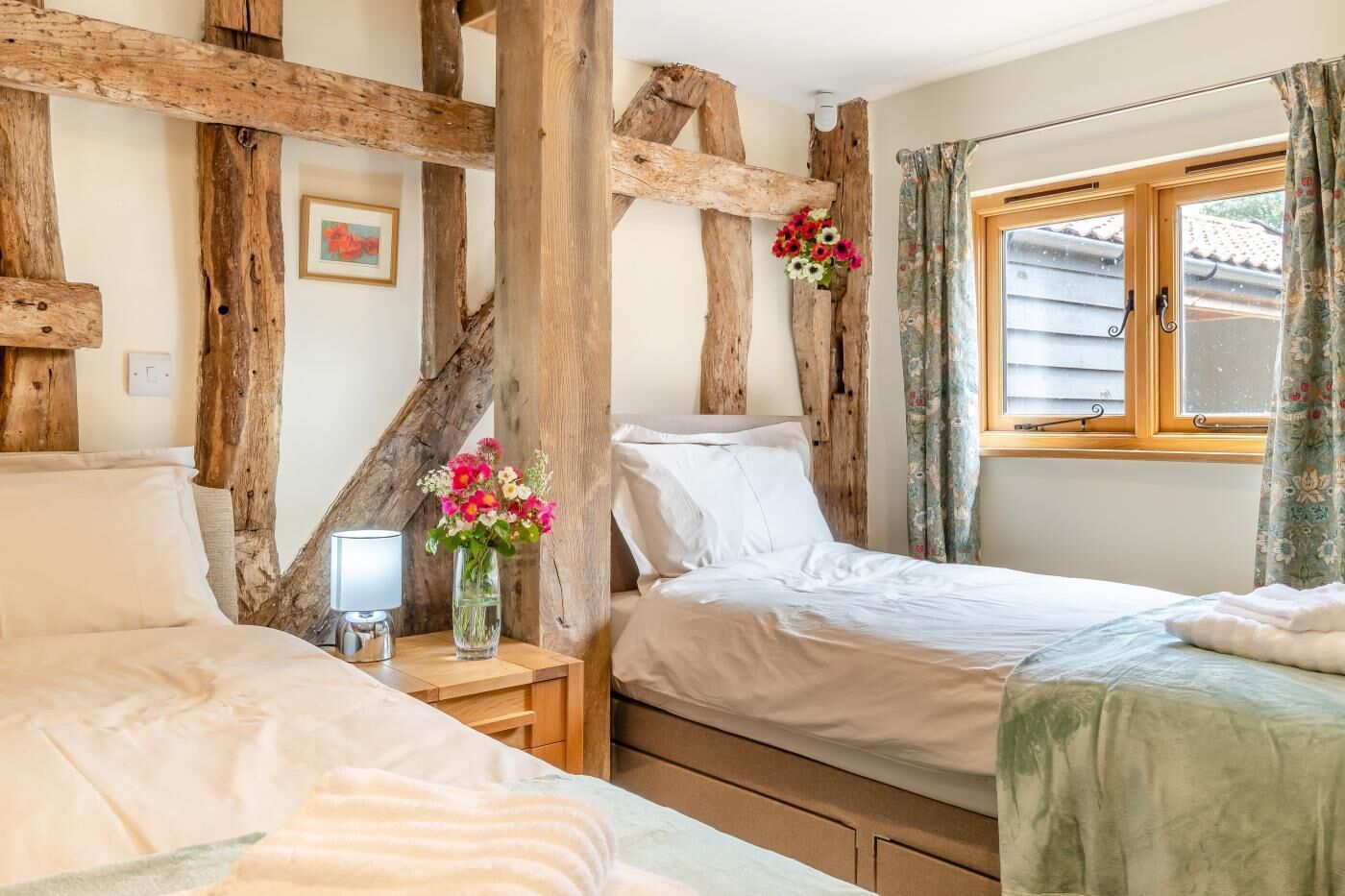 Un dormitorio con dos camas, vigas de madera, una mesita de noche con lámpara y una ventana con cortinas.