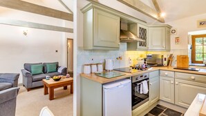 A compact kitchen with a built-in oven, a coffee maker, and a dining area with a sofa and table. - 2 Bed in Hayle (oc-l42842) (Saint Erth Praze)