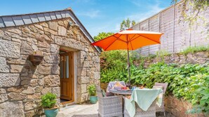 A stone building with a wooden door, a patio with wicker furniture, and an orange umbrella. - 2 Bed in Hayle (oc-l42842) (Saint Erth Praze)