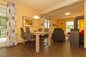 A dining area with a table, chairs, a hanging light fixture, and a view of the outdoors. - Fewo 7.0.N - Ferienwohnung in Graal-Müritz (Graal-Müritz)