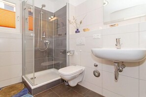 A modern bathroom with a glass-enclosed shower, a white toilet, and a white sink. - Fewo 7.0.N - Ferienwohnung in Graal-Müritz (Graal-Müritz)