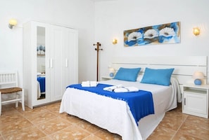 Ein Schlafzimmer mit Bett, Schrank, Bank, Nachttisch und einem Wandbild.