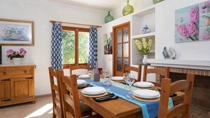 A dining area with a wooden table set for four, surrounded by chairs, with a fireplace and decorative items on the wall. - VILLA CAN TORRETA (Pollensa)