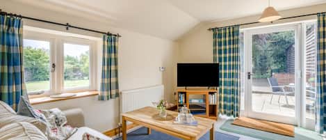 Una sala de estar acogedora con un sofá, una mesa de centro y un televisor. Hay cortinas en las ventanas y una puerta que da a un espacio exterior.