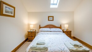 Ein Schlafzimmer mit einem Bett, zwei Nachttischen, einem Fenster und zwei gerahmten Bildern an der Wand.