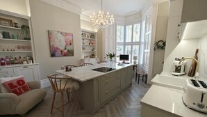 Ett modernt kök med en central köksö, en matplats med en soffa och ett stort fönster som släpper in naturligt ljus.