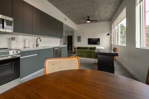 A modern kitchen with grey cabinets, a wooden dining table, and a green sofa in the living area. - Brand New Spacious 1 bedroom in Wynwood (Miami)