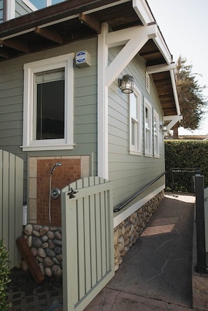 A residential building with a covered porch, a stone wall, and a gated entrance. - Capitola Pelican House (Capitola)
