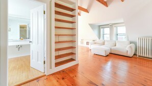 Una habitación amplia con suelos de madera, un sofá blanco y una estantería empotrada de madera.
