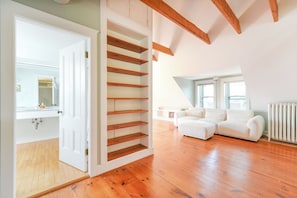 Ein geräumiges Zimmer mit Holzböden, einem weißen Sofa und einer eingebauten Holzregaleinheit.