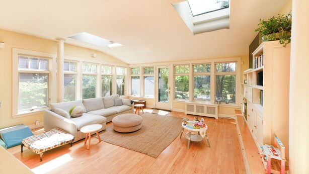 Amplia sala de estar con sofá, reposapiés y una mesita, ventanas grandes y tragaluces.