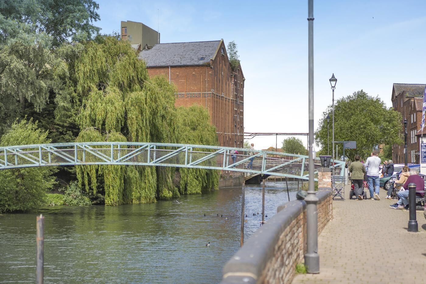A pedestrian bridge over a river with trees and buildings in the background.
