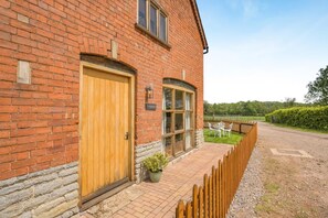 A brick building with a wooden door and windows, a paved pathway, and a fenced garden area. - 1 Bed in Longdon (oc-f42452) (Yardebridge)
