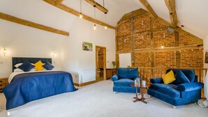 Quarto com uma cama grande, dois sofás azuis, uma mesa pequena e vigas de madeira aparente.