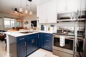 A modern kitchen with dark blue cabinets, stainless steel appliances, and pendant lighting.