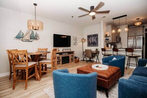 A modern living room with a dining area, a TV, and a kitchen in the background.
