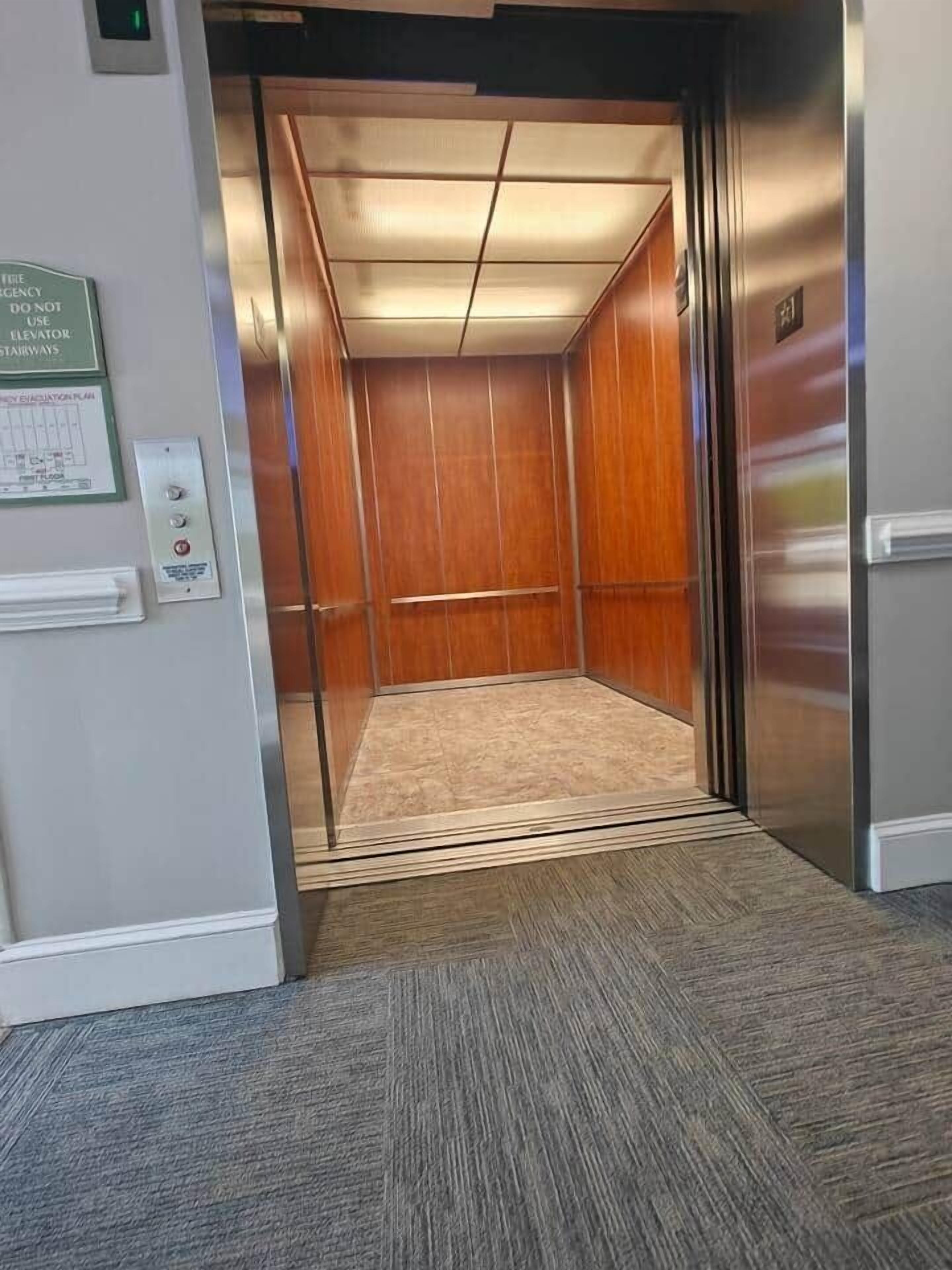 An elevator interior with a wooden finish, a control panel, and a carpeted floor.