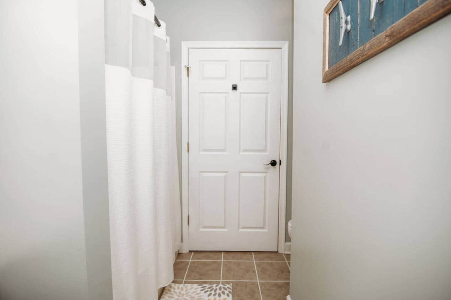 A hallway with a white door, a shower curtain, and a tiled floor.
