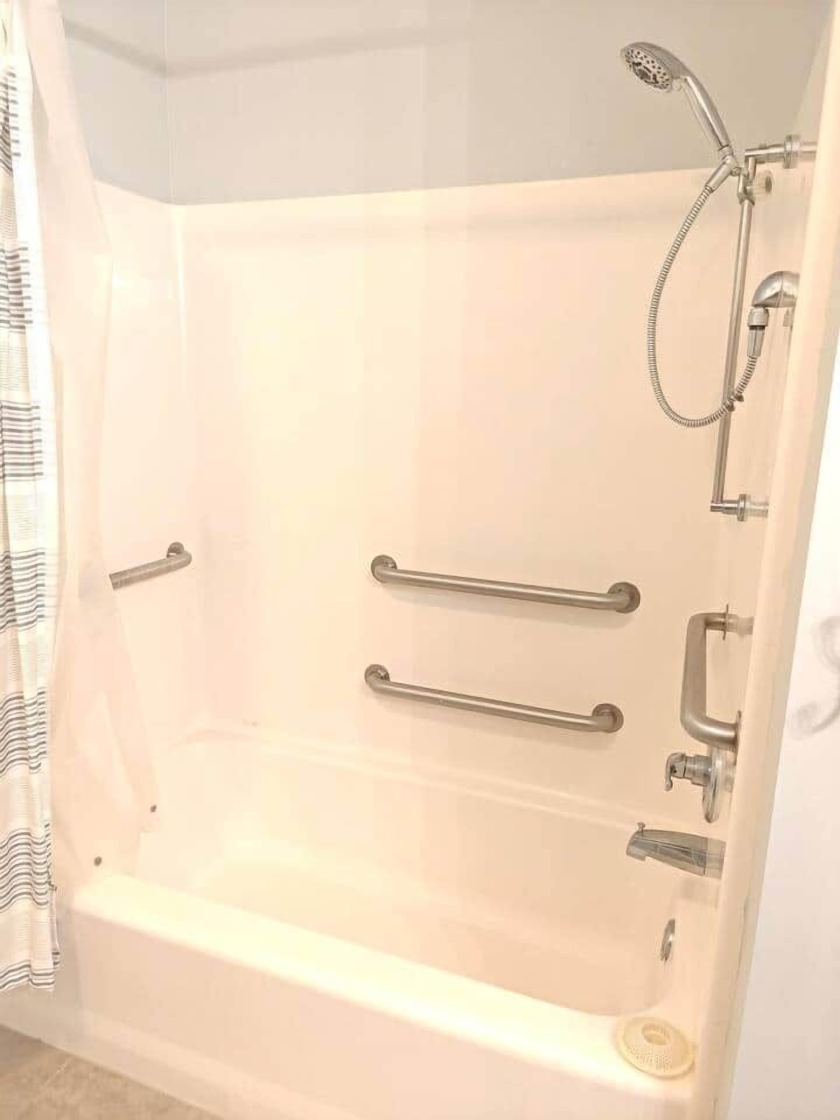 Eine weiße Badewanne mit Handläufen, einer Duschbrause und einem separaten Duschkopf.