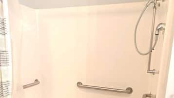Eine weiße Badewanne mit Handläufen, einer Duschbrause und einem separaten Duschkopf.