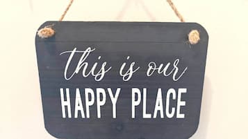 A dark wooden sign with the text 'this is our HAPPY PLACE' in white letters, hanging on a wall.