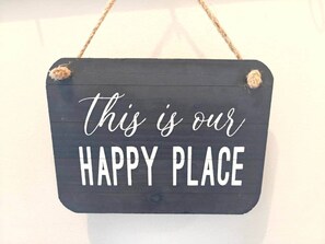 Ein dunkles Holzschild mit dem Aufdruck 'this is our HAPPY PLACE' in weißen Buchstaben, an einer Wand befestigt.