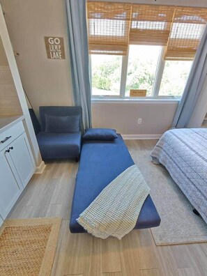 Quarto compacto com uma cama de solteiro, um pequeno espaço para sentar e uma janela com vista para o exterior.