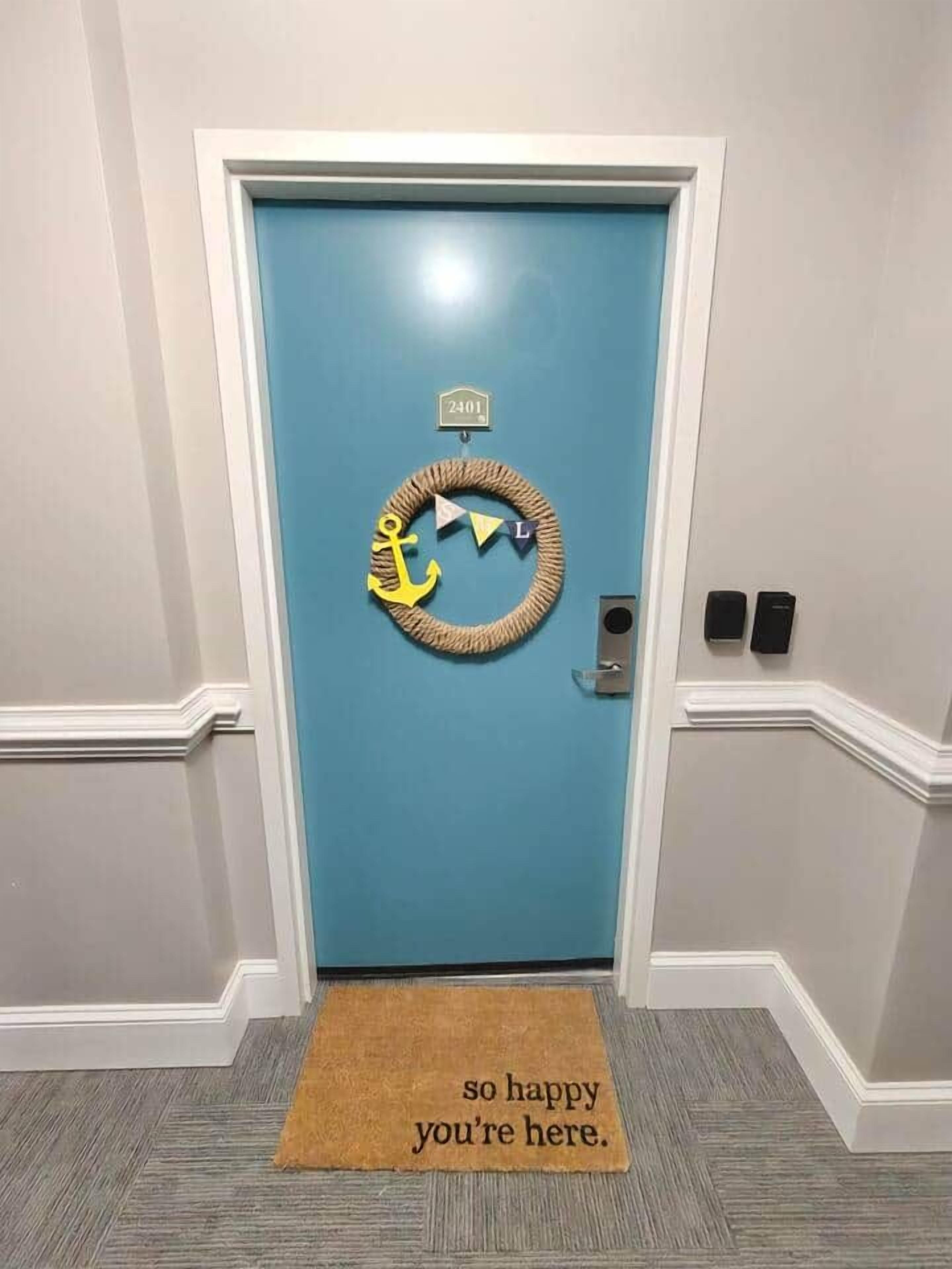 Une porte bleue ornée d’une guirlande, un paillasson avec une inscription et une sonnette.