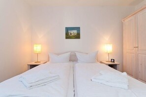 Ein Doppelbett mit weißer Bettwäsche, zwei Nachttische mit Lampen, ein gerahmtes Bild an der Wand und ein Holzschrank.