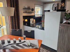 Eine kleine Küche mit Essbereich, einem Kühlschrank und einem Fenster mit Vorhängen.