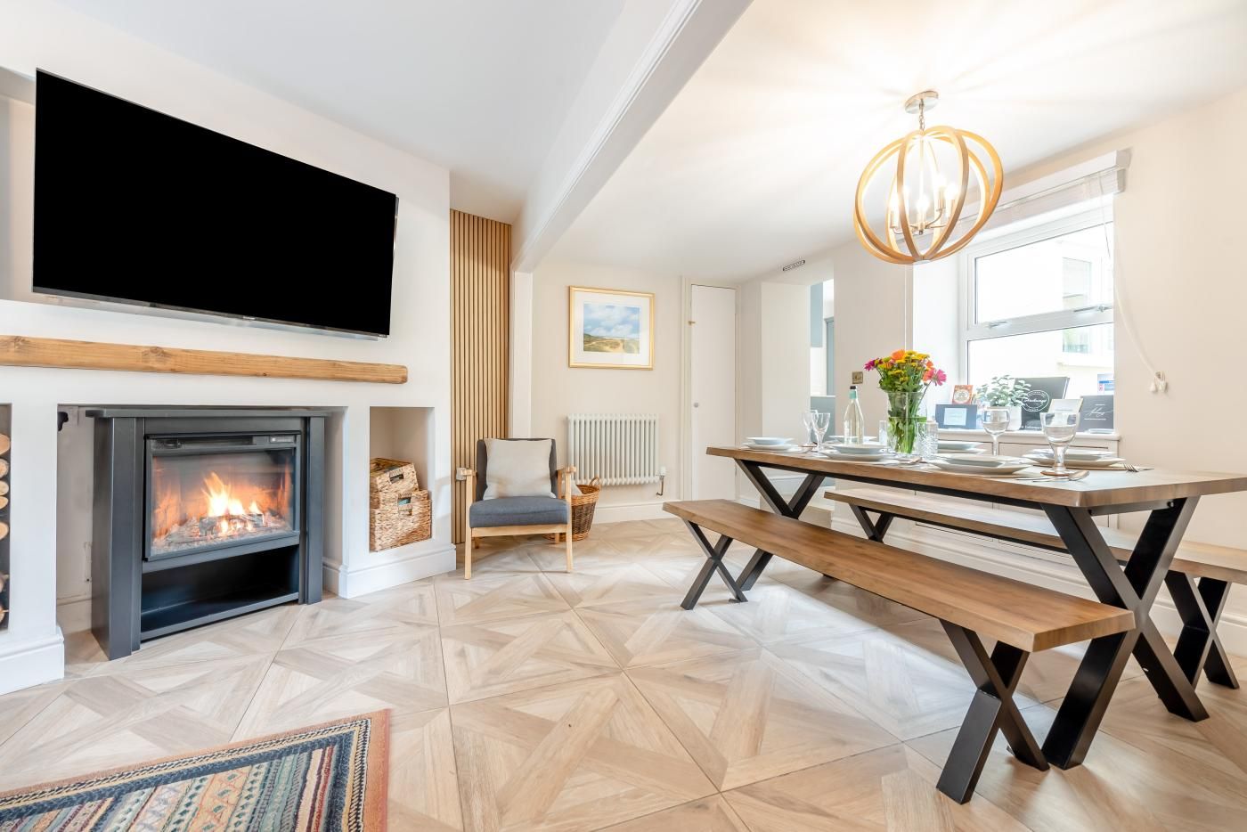 A modern living room with a fireplace, a dining table set for two, and a television mounted above the fireplace.
