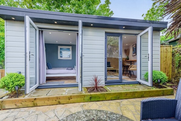 Ein modernes, eingeschossiges Haus mit offener Wohnbereitschaft, einem Schlafzimmer mit Bett und Fenster sowie einem Essbereich mit Tisch und Stühlen.