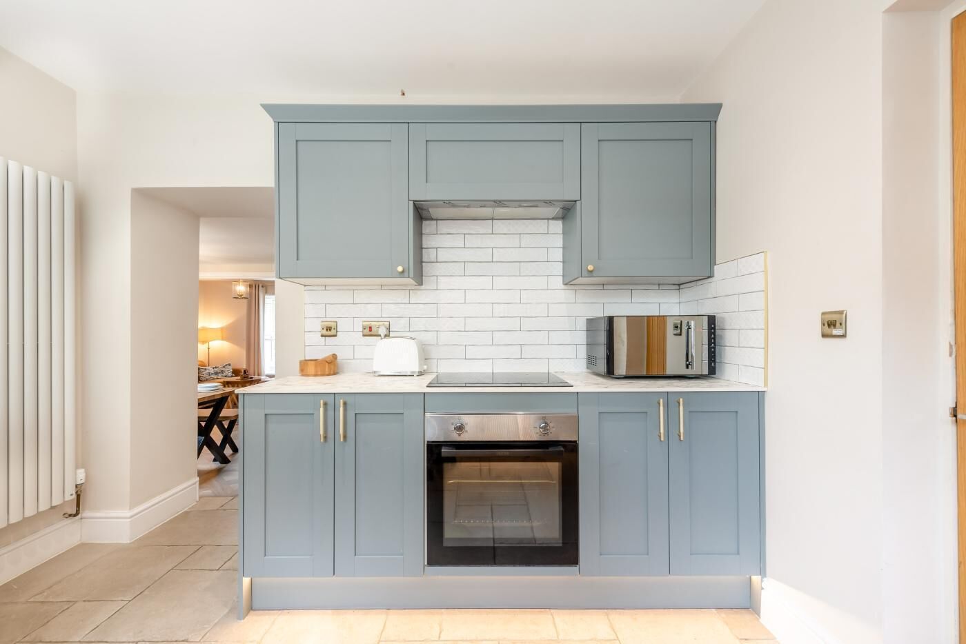 Una cocina con armarios azul claro, salpicadero de azulejos blancos, horno empotrado y microondas.