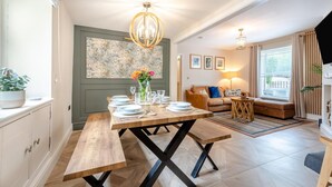 A dining area with a wooden table set for four, a sofa, a small side table, and a painting on the wall. - 4 Bed in Tenby (oc-a42730) (Tenby)