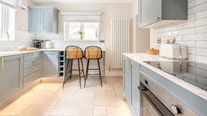 A modern kitchen with grey cabinets, a white countertop, two bar stools, a toaster, and a radiator. - 4 Bed in Tenby (oc-a42730) (Tenby)