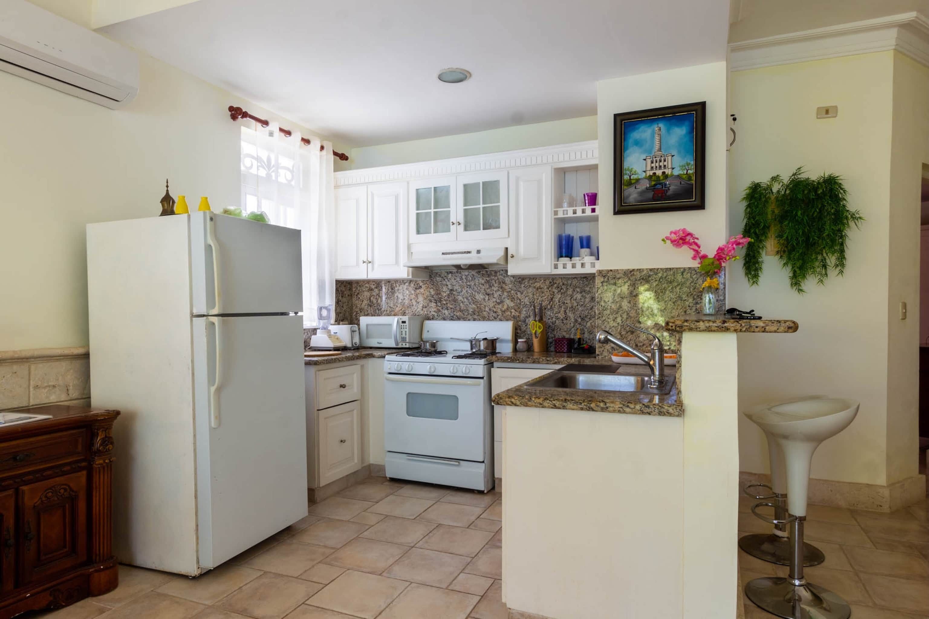 A kitchen with white cabinets, a refrigerator, a stove, a microwave, and a sink.