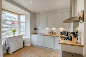 Eine moderne Küche mit weißen Schränken, einer Holzarbeitsplatte, einem eingebauten Backofen und einem Fenster mit Jalousien.