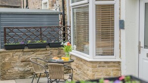 A patio with wicker chairs, a table with breakfast, and flower pots. - 3 Bed in Skipton (oc-h42831) (Skipton)