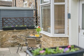 Eine Terrasse mit Korbstühlen, einem Tisch mit Frühstück und Blumentöpfen.