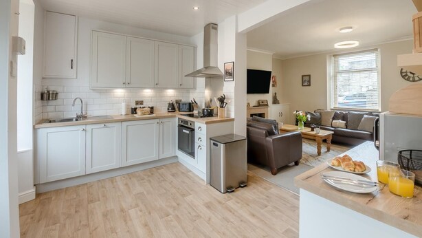 A modern kitchen with white cabinets, a built-in oven, and a dining area with a sofa and table. - 3 Bed in Skipton (oc-h42831) (Skipton)