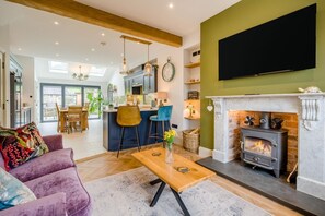 Ein Wohnzimmer mit Kamin, einem an der Wand befestigten Fernseher und einer Küche im Hintergrund.