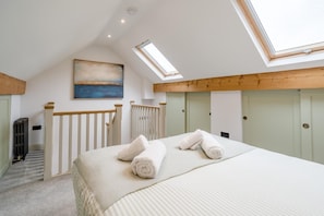 Ein Schlafzimmer mit Dachfenster, einem Gemälde, einem Bett mit Handtüchern, einem Heizkörper und einer Treppe.