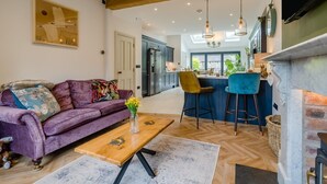 En moderne stue med en lilla sofa, et træbord og et køkkenområde med bar og høje lofter.