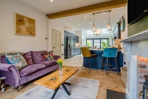 Ein modernes Wohnzimmer mit einem violetten Sofa, einem Holztisch und einer Küchenzeile mit Bar und hohen Decken.