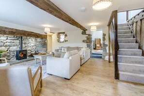 Ein gemütliches Wohnzimmer mit Kamin aus Stein, Holzbalken, einer Treppe und einem Sofa.