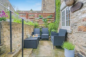 A narrow courtyard with wicker furniture, potted plants, and a stone wall. - 2 Bed in Leyburn (oc-l42746) (Leyburn)
