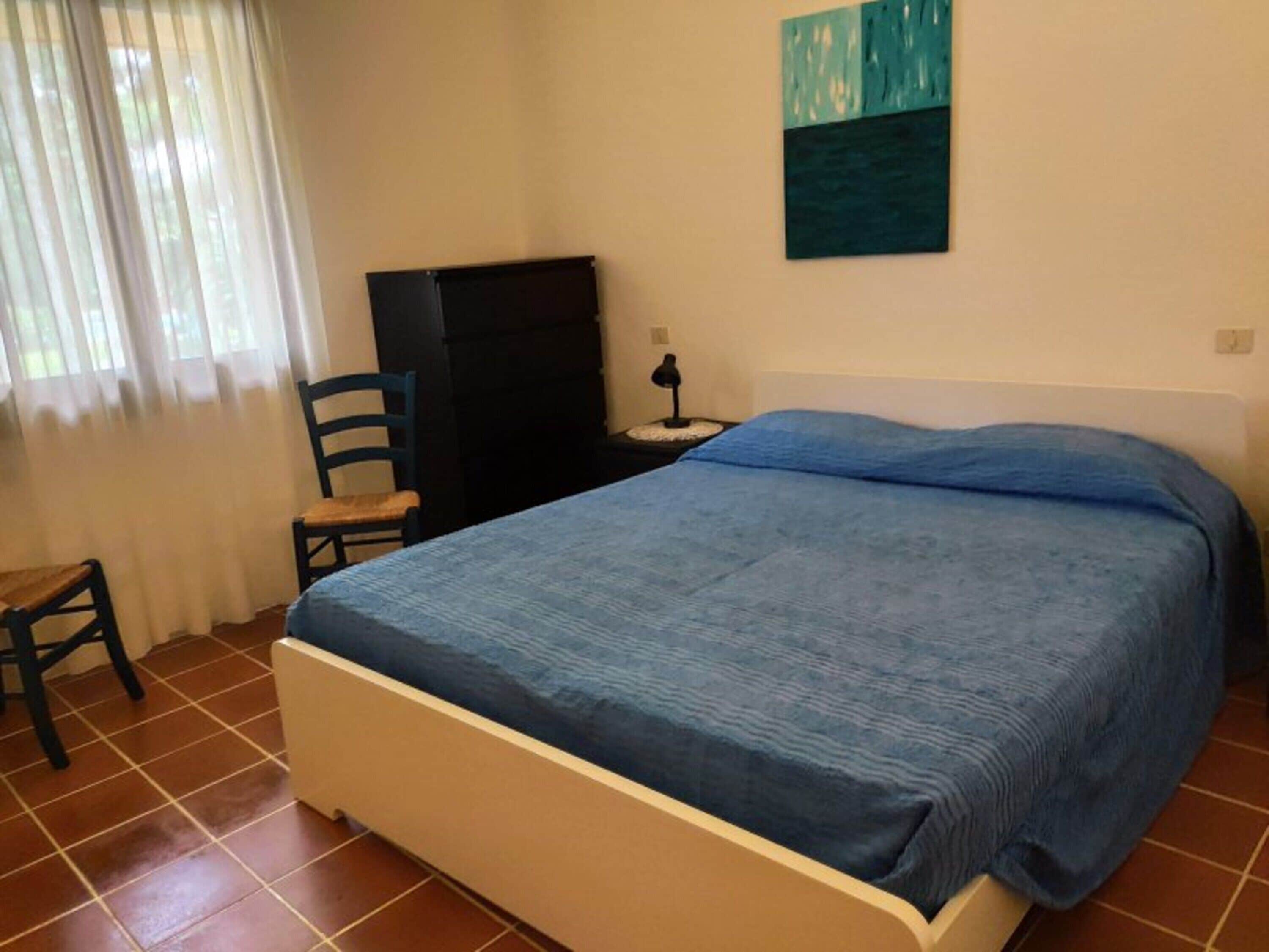 A bedroom with a bed, a chair, a desk, and a painting on the wall.