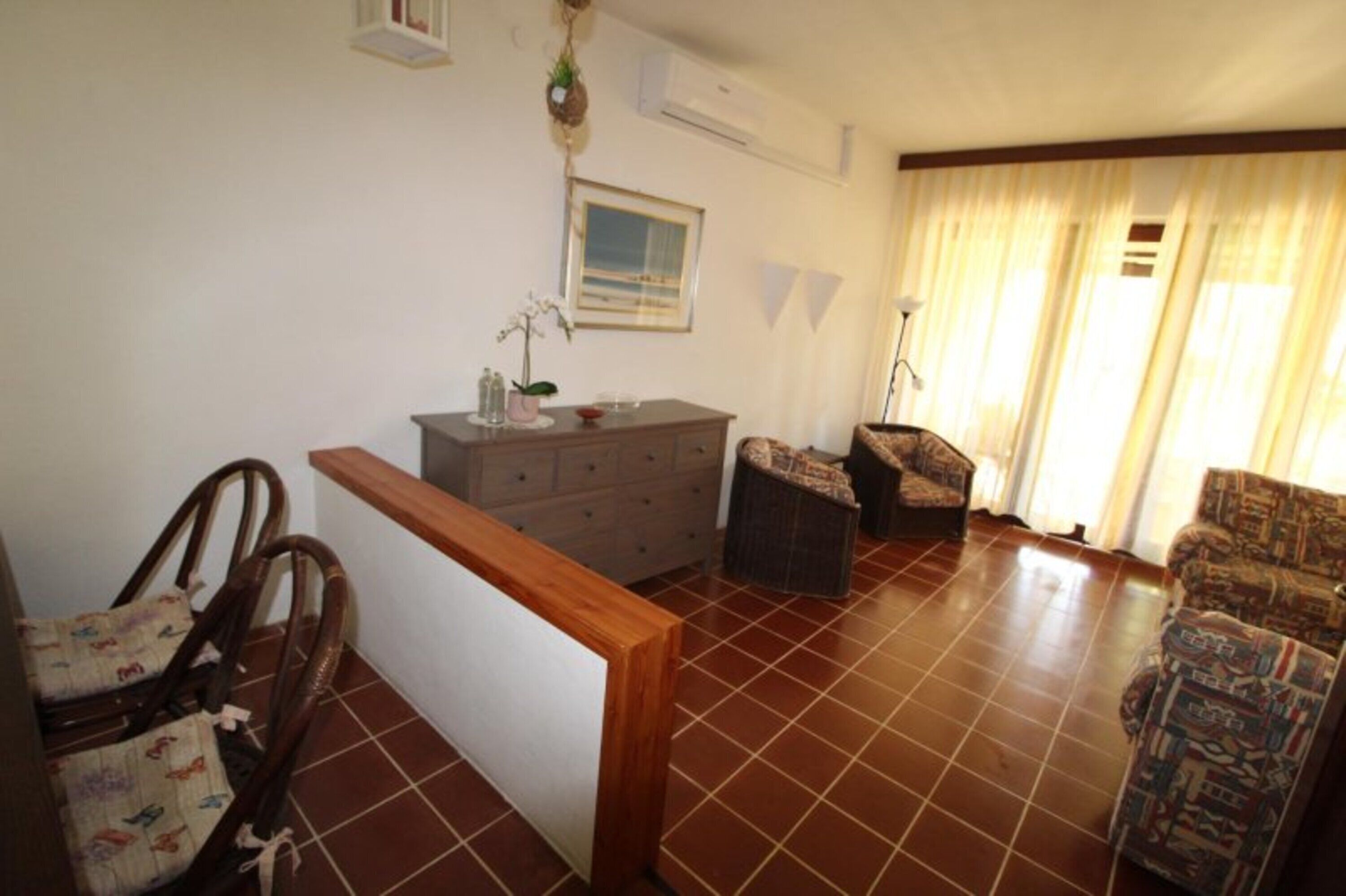 A living room with a wooden bench, a sofa, a dining table with chairs, a cabinet, and a window with curtains.