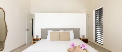 Une chambre à coucher avec un lit, des tables de chevet, un miroir et une fenêtre avec des stores.